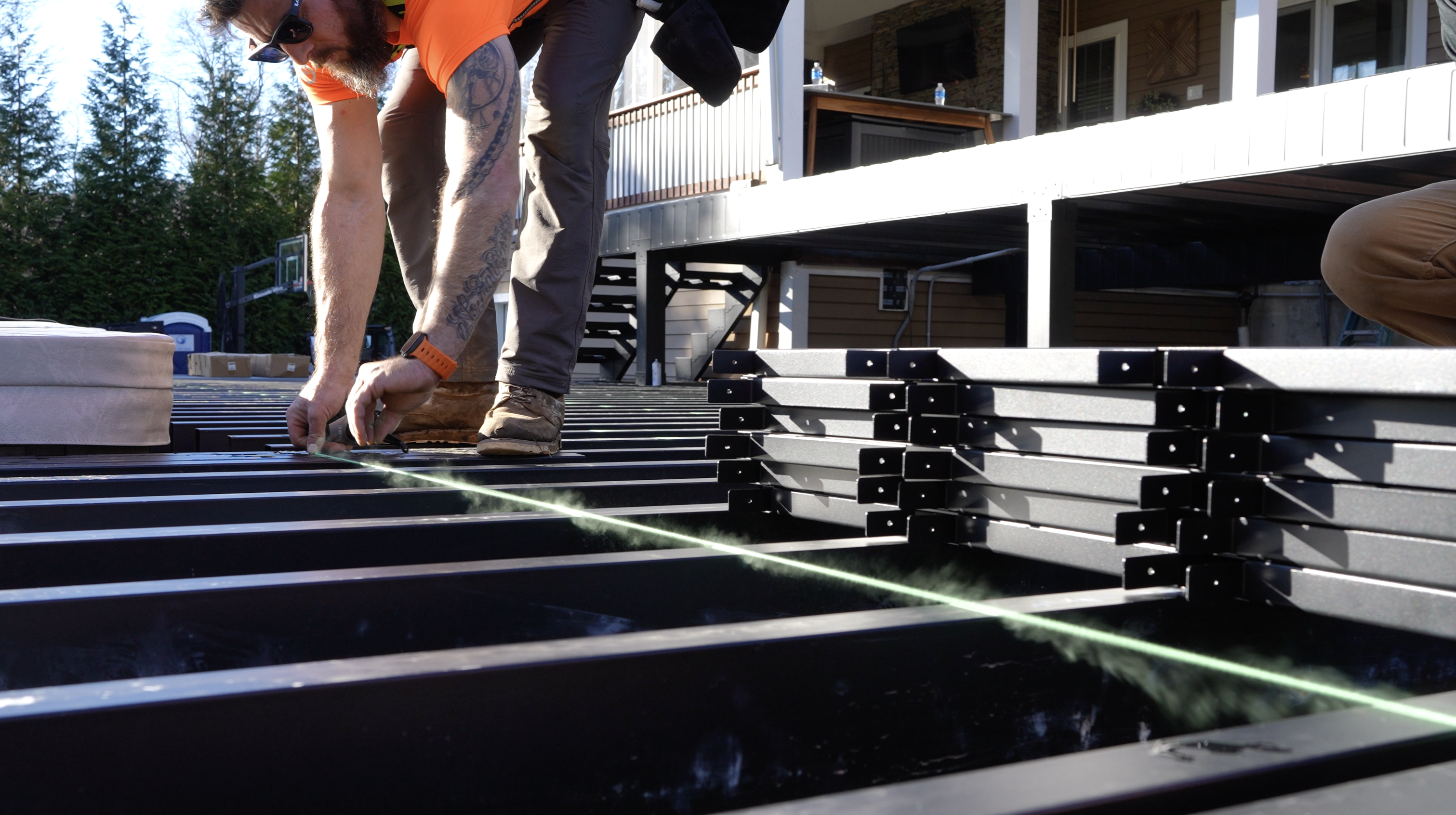 A contractor installs Fortress Evolution steel deck framing, using string for precise alignment to create a durable and fire-safe foundation for outdoor spaces.