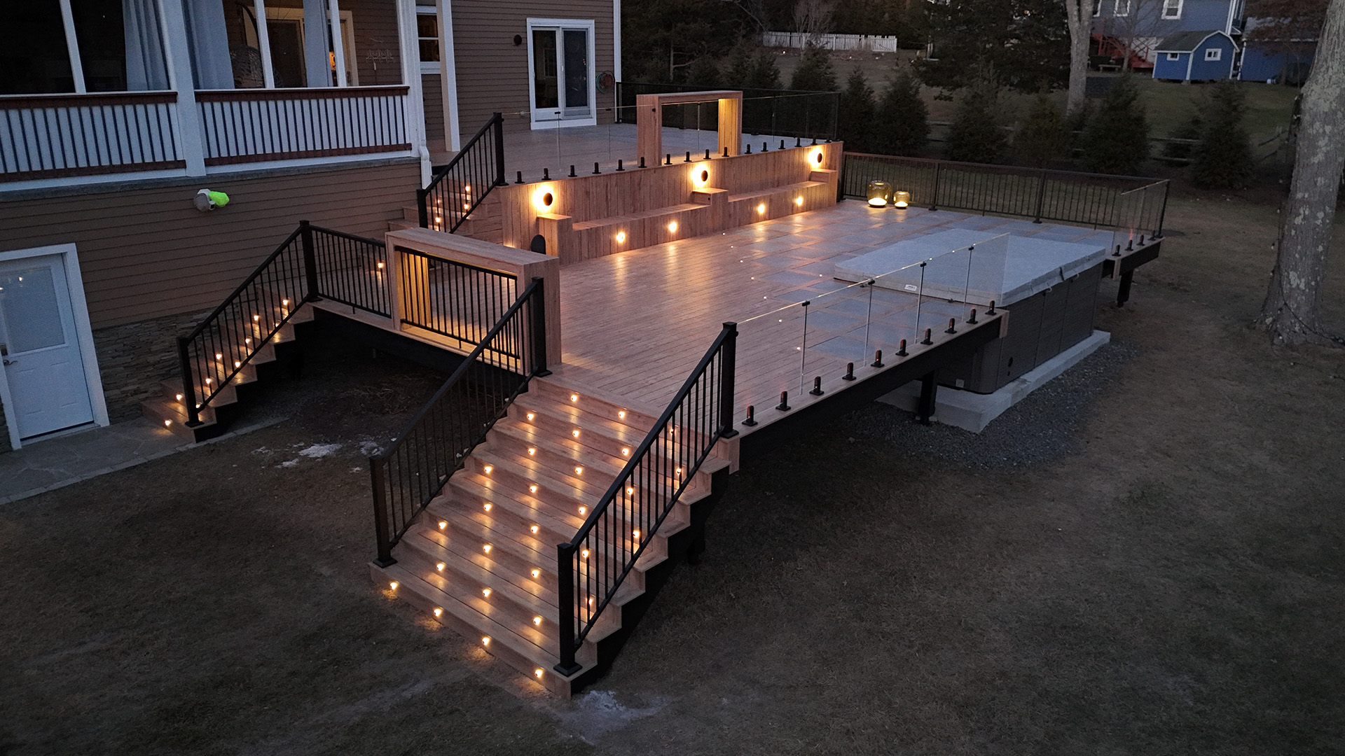 Modern multi-level deck illuminated with integrated stair and railing lights, framed with black steel joists.
