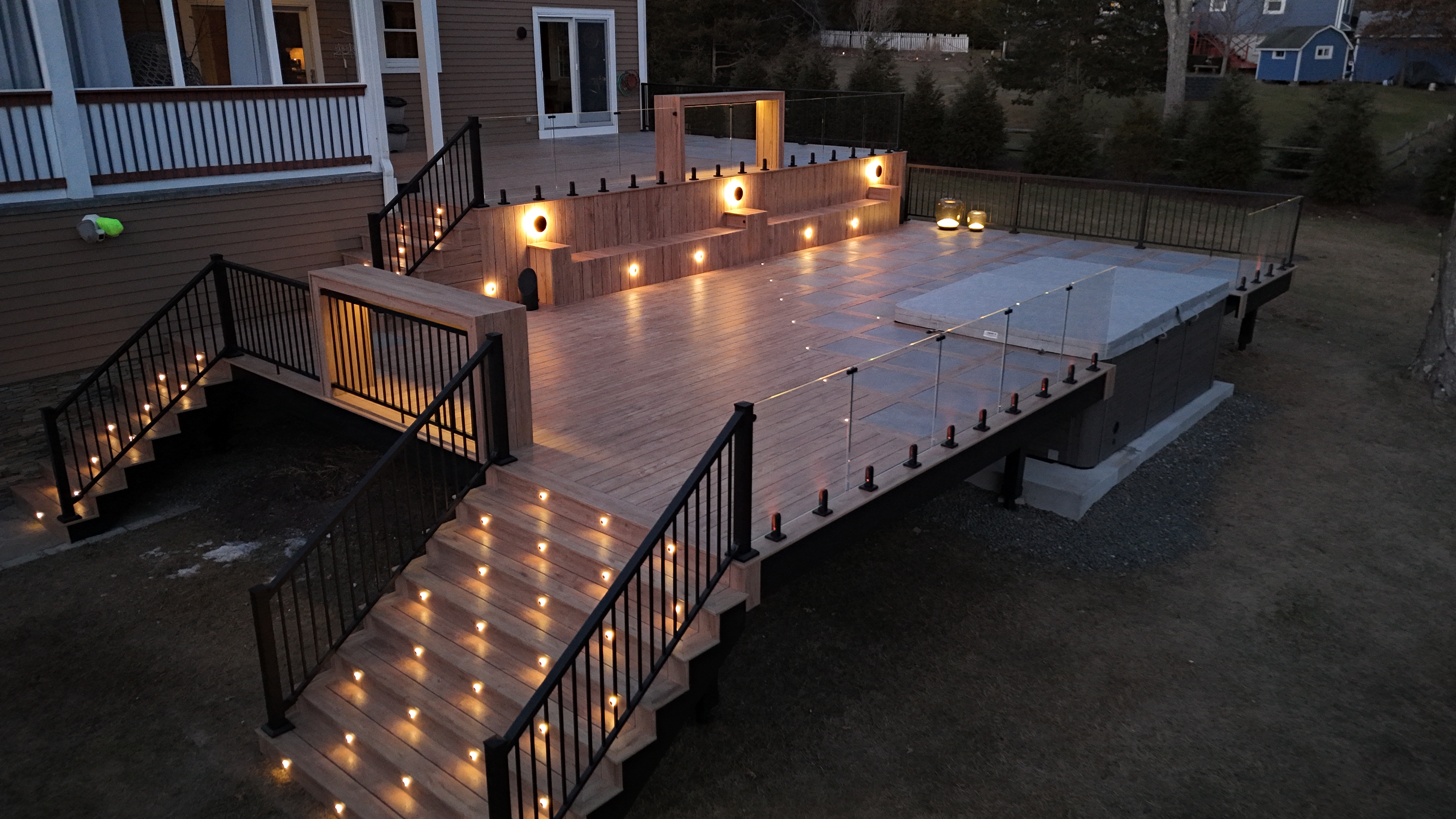 A modern, elevated deck built with Fortress steel framing, featuring deck post lights, glass railing, and tile pavers, creating a stylish and durable outdoor space.